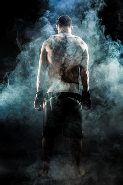 Muscular kickbox or muay thai fighter with tattoo standing back in smoke. - Photo, image
