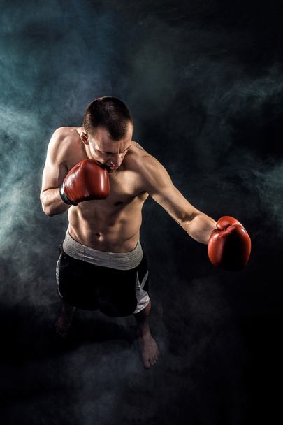 Muscular kickbox or muay thai fighter punching in smoke. - Фото, изображение