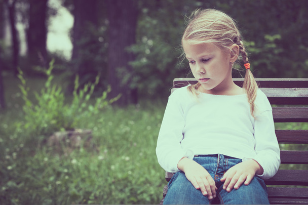 Portrait of sad blond little girl sitting on bench - Foto, imagen
