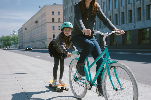 Mother and daughter ride a scooter and bicycle together - Foto, imagen