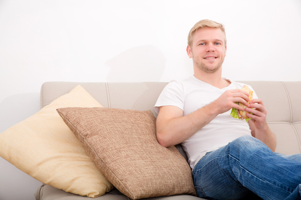 Young man eating a sandwich at home - Valokuva, kuva