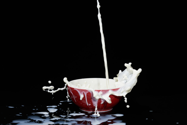 Caduta flusso di latte in ciotola rossa creando molti spruzzi e vortice
. - Foto, immagini