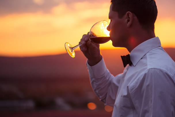 Élégant jeune homme qui boit du vin au coucher du soleil
 - Photo, image