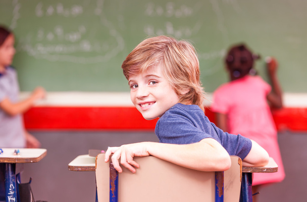 Hymyilevä poika koulussa istuu luokkahuoneessa
 - Valokuva, kuva