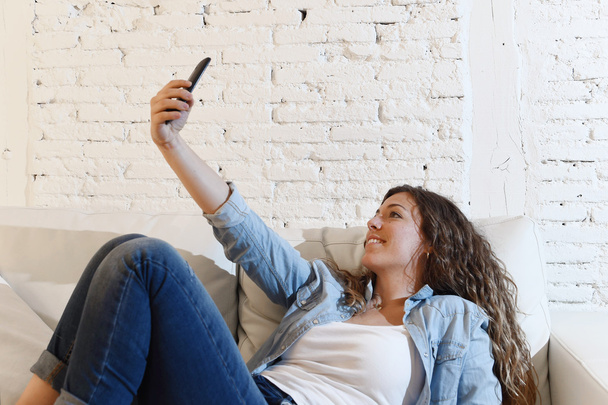 young attractive hispanic woman lying on home couch taking selfie photo with mobile phone having fun - Fotó, kép