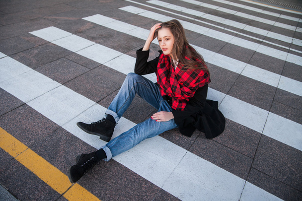 Portrait of brunette in stylish coat sitting on crosswalk - Фото, изображение