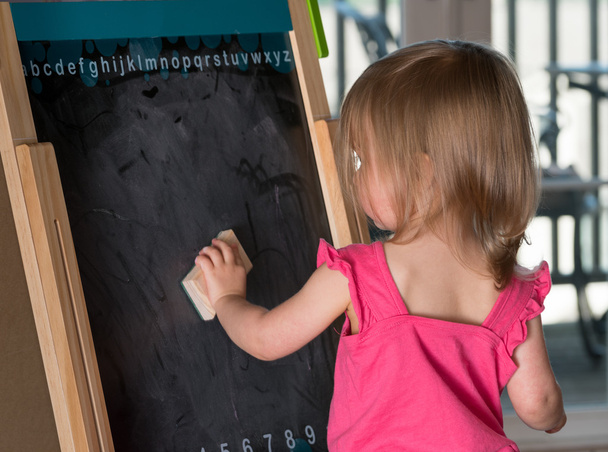 Young baby girl cleaning a blackboard - Photo, Image