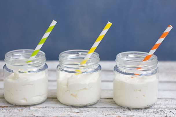 Yogurt in three small jars with straws. On a white board - Photo, Image