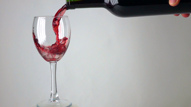 Man pouring red wine into a glass against gray background, super slow motion - Video