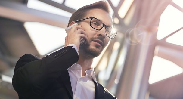 Portrait of handsome businessman in suit and eyeglasses speaking on the phone in airport - Photo, Image