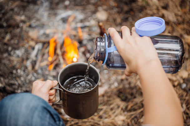 man traveler pours water from a bottle into a metal mug.  - 写真・画像