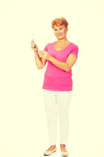 Smiling senior woman holding toothpaste and toothbrush - Photo, Image