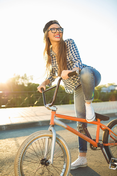 Preciosa mujer joven en un sombrero montando una bicicleta en el fondo de la ciudad
  - Foto, Imagen