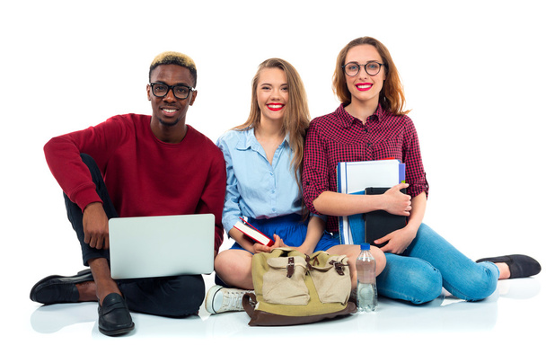 Three students sitting with books, laptop and bags isolated on w - Photo, Image