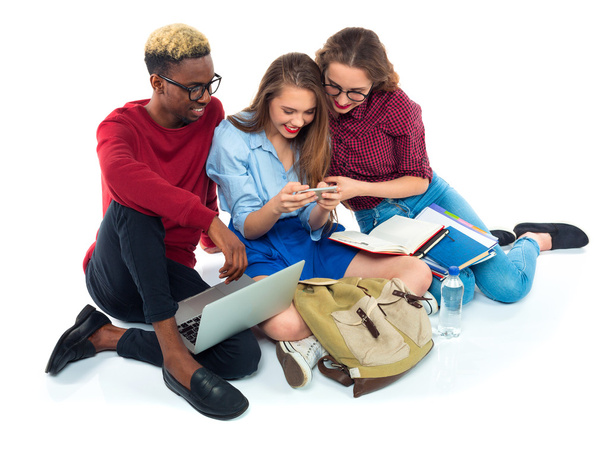 Three students sitting with books, laptop and bags isolated on w - Photo, Image