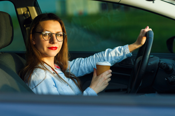 Молода жінка з кавою, щоб піти за кермом своєї машини
 - Фото, зображення