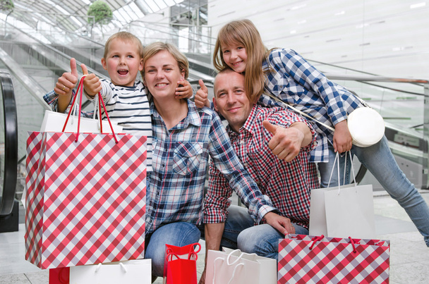 Семья с сумками в торговом центре показывает большие пальцы
  - Фото, изображение