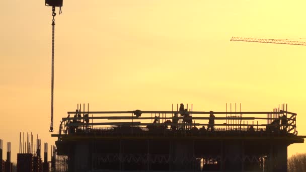 Sylwetki pracowników budowlanych przeciwko pomarańczowe niebo. 4 k teleobiektywu strzał - Materiał filmowy, wideo