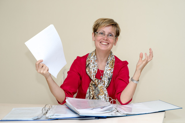 portrait d'une femme d'affaires heureuse avec des papiers assis sur le bureau et tenant une feuille de papier
 - Photo, image