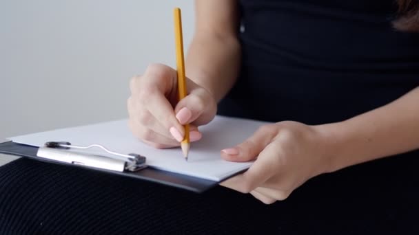 Close-up of a female hand writing on an blank notebook with a yellow pencil - Materiaali, video