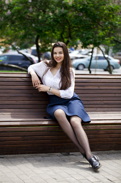 Young beautiful girl sitting on a bench in the summer park - Valokuva, kuva