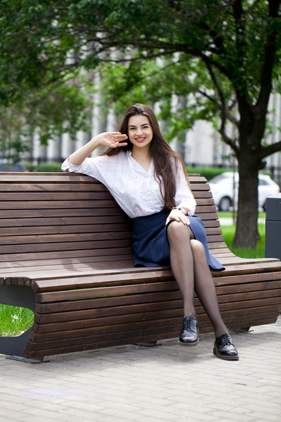 Young beautiful girl sitting on a bench in the summer park - Photo, Image