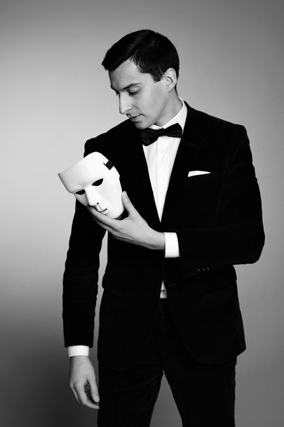Tief in Gedanken erfolgreicher, gut aussehender junger Mann im Kostüm mit weißer Maske. Schwarz-Weiß-Bild. - Foto, Bild