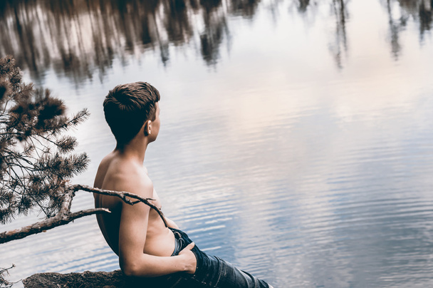 Έφηβος, κοντά στη λίμνη κάθεται πάνω σε ένα βράχο - Φωτογραφία, εικόνα