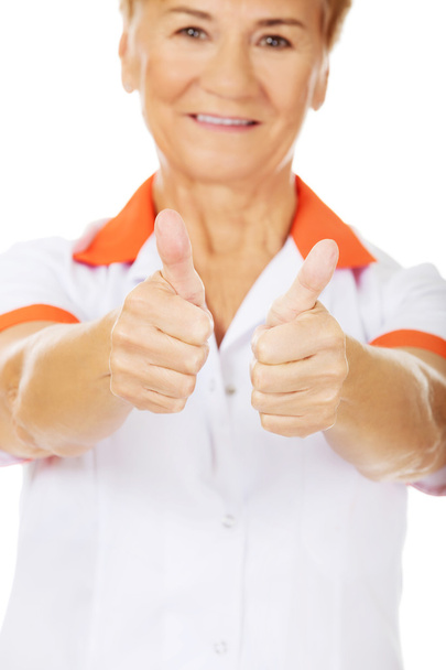 Smile elderly female doctor or nurse shows thumbs up - Foto, imagen