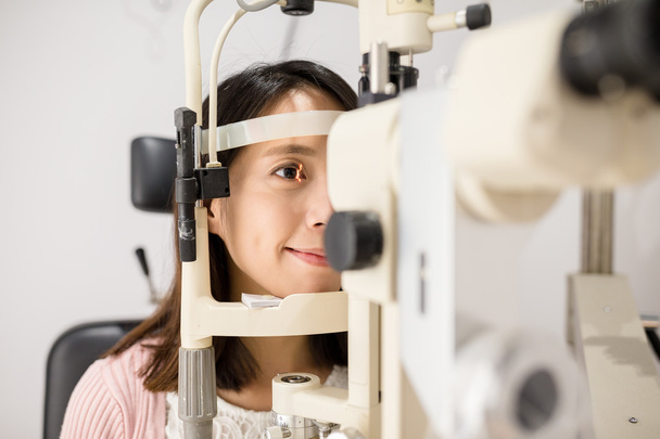 Nainen katsoo oftalmoskooppiin.
 - Valokuva, kuva