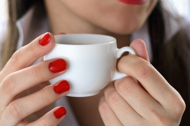 Una chica con una camisa blanca bebiendo café de una taza blanca. Primer plano de los labios. Macro con desenfoque y enfoque suave
. - Foto, imagen