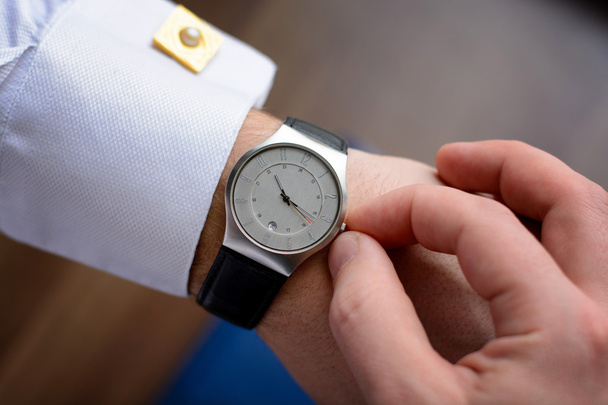 Hand of a man in white shirt with gold cufflinks with clock on a wooden desk with a notebook, fountain pen - 写真・画像