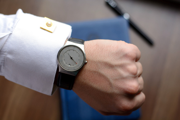 Рука чоловіка в білій сорочці з золотими запонки з годинником на дерев'яному столі з блокнотом, ручкою для фонтану
 - Фото, зображення