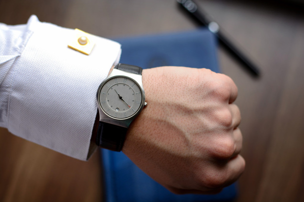 Hand of a man in white shirt with gold cufflinks with clock on a wooden desk with a notebook, fountain pen - Photo, image