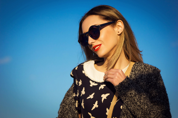 Beautiful young woman in sunglasses against blue sky - Foto, afbeelding