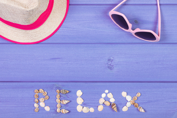 Word relax made of seashells, sunglasses and straw hat on purple boards, summer time, copy space for text - Photo, Image