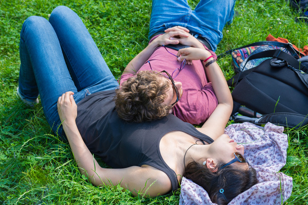 Young adult couple lying down on lush green grass in park, relaxing, embracing. Real people, natural color. Conpept of happy relationship and summer lifestyle. - Photo, Image