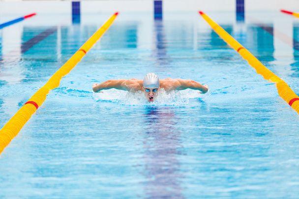 dynamic and fit swimmer in cap breathing performing the butterfly stroke - Fotoğraf, Görsel