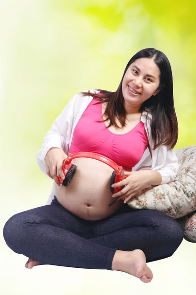 Boldog terhes nő, állítva, hogy a fejhallgató a hasában  - Fotó, kép
