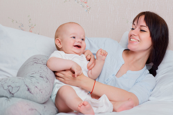 Happy baby plays with mum in pajamas on the bed, laughing and sm - Fotografie, Obrázek