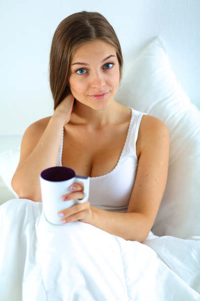 A pretty young woman in bed enjoying a cup of tea - Foto, imagen