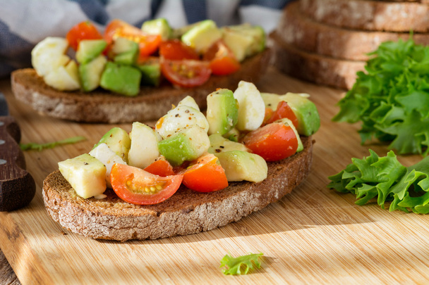 Healthy appetizer bruschetta with avocado, tomato and mozzarella - Foto, afbeelding