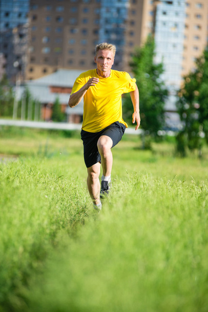 Sporty man jogging in city street park. Outdoor fitness. - Фото, изображение