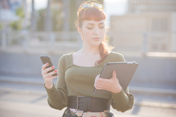 Κοκκινομάλλης γυναίκα χρησιμοποιώντας ένα smartphone και tablet - Φωτογραφία, εικόνα