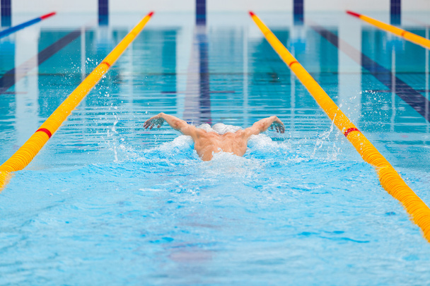 dynamic and fit swimmer in cap breathing performing the butterfly stroke - Foto, afbeelding