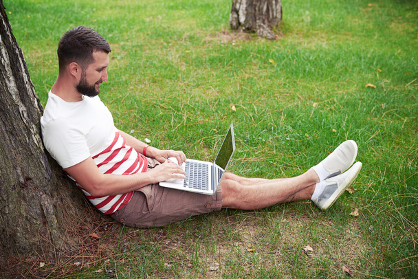 Young bearded man with laptop in the garden - Φωτογραφία, εικόνα