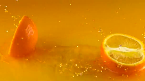 Orange hits orange juice surface and splits into halves. Slow motion video - Кадры, видео