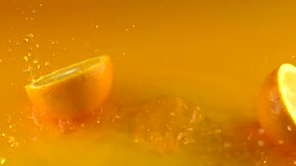 Orange falls on orange juice surface and splits into halves. Slow motion video - Кадры, видео