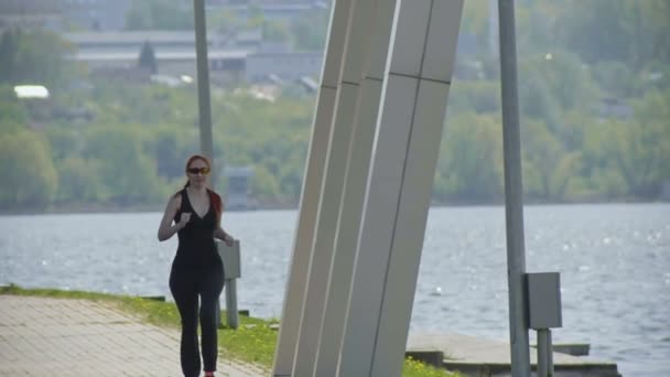 Nuori kunto nainen juoksee puistossa, lähellä jokea, telephoto. Valkoihoinen malli. Hidastus
 - Materiaali, video