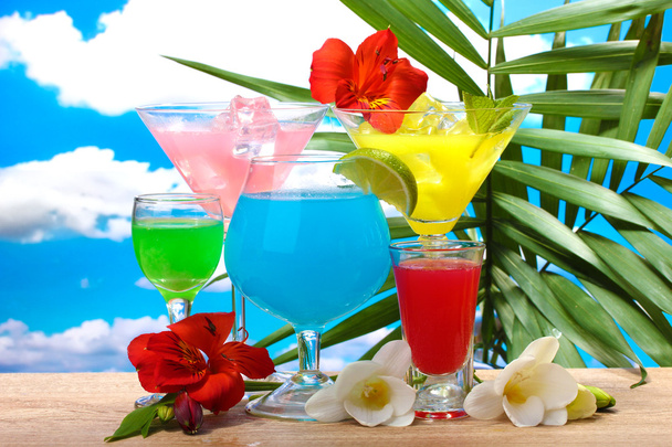Exotic cocktails and flowers on table on blue sky background - Foto, afbeelding